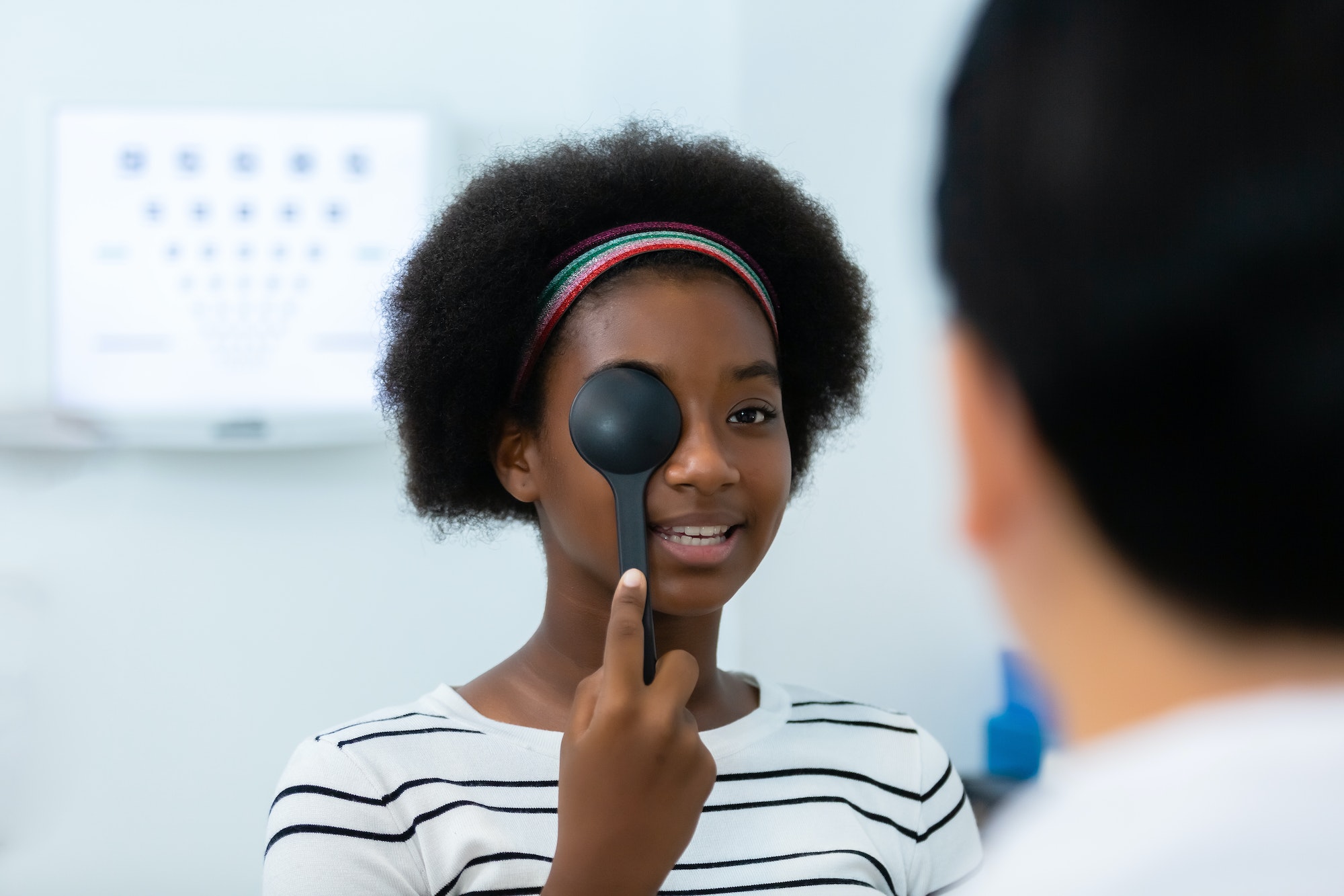 Young woman african american using occluder for eye test ophthalmological in optics clinic.