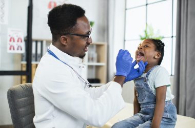 Afro-american child girl at doctor's office, handsome black male doctor examining her throat