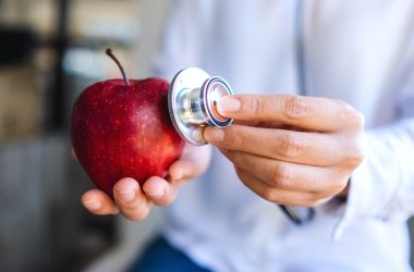Closeup image of a doctor using stethoscope to examine a red apple